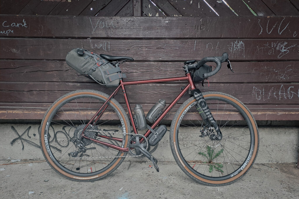 Rower gravelowy z torbami bikepackingowymi przy drewnianym przystanku autobusowym