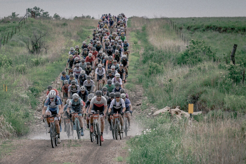 Grupa rowerzystów na gravelach jadących szutrową drogą za chmurą kurzu